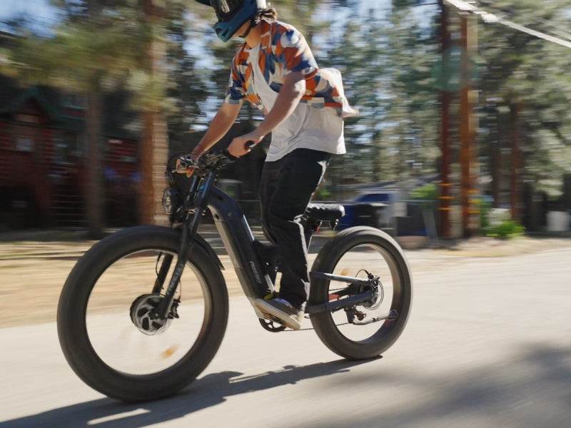 Rider standing on the pedals of a blue-gray Freesky Warrior Ultra M-530 at speed on a paved forest road — Zeus eBikes Canada
