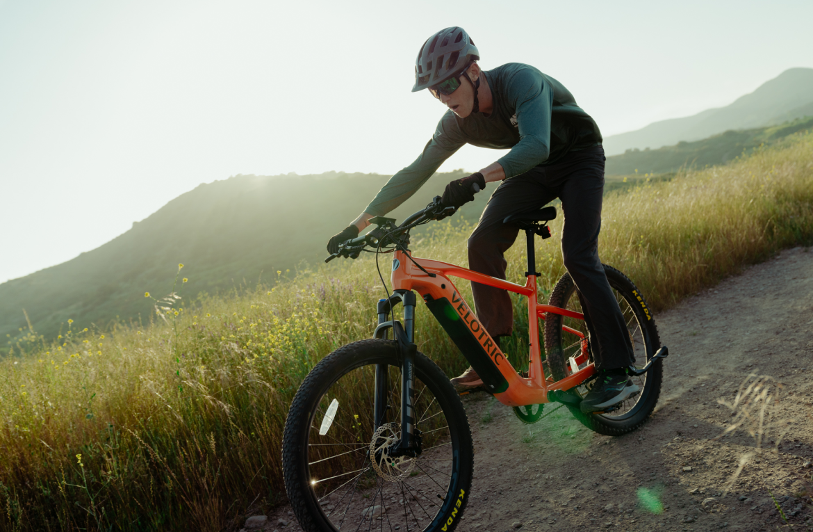 Rider on a Velotric Summit 1 in Sunrise Orange on a grassy hillside trail (Velotric photo) — Zeus eBikes Canada