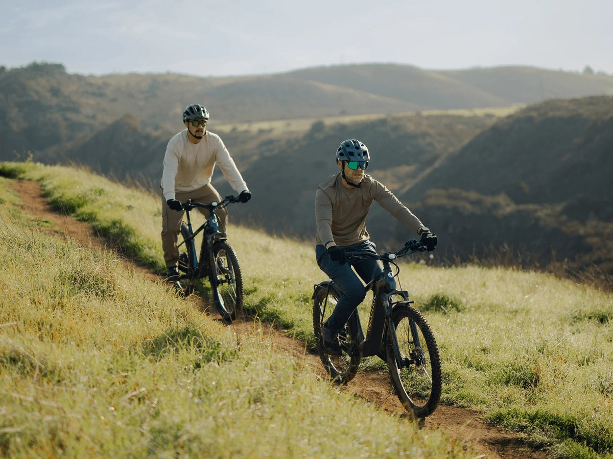 Two riders on Velotric Summit 2 e-bikes on a grassy hillside trail (Velotric photo) — Zeus eBikes Canada