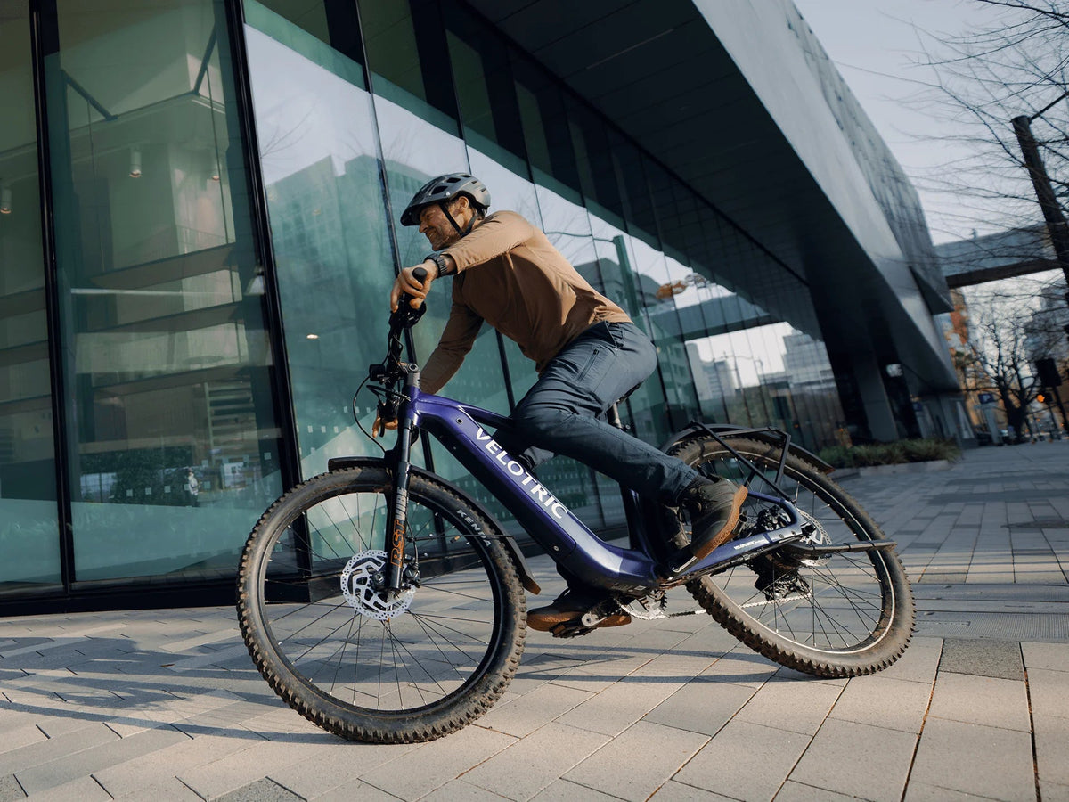 Rider on a Velotric Summit 2 beside a glass building in the city (Velotric photo) — Zeus eBikes Canada