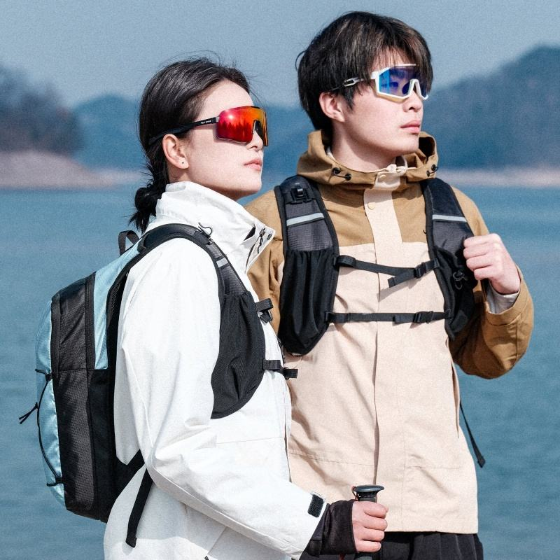 Two people by a lake wearing the West Biking hydration backpack: one seen from the side in Blue, one from the front showing the shoulder-strap harness — Zeus eBikes Canada
