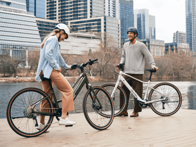 Two riders with Velotric Tempo e-bikes by a river in the city (Velotric photo) — Zeus eBikes Canada