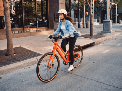 Rider on a Velotric Tempo Mid-Step in Sunset Tangerine on a city street (Velotric photo) — Zeus eBikes Canada
