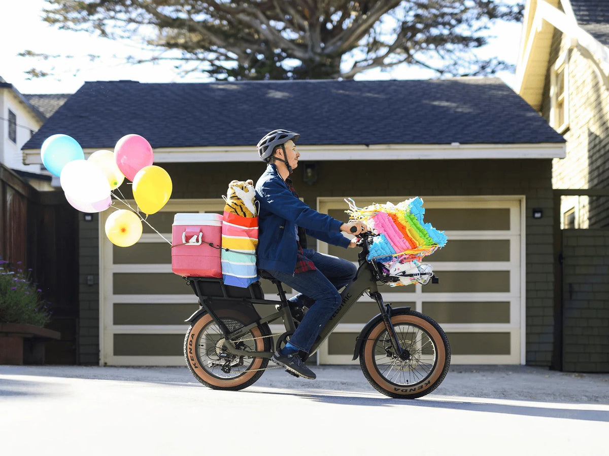 Rider on a Velotric GoMad carrying a child passenger and balloons past a house (Velotric photo) — Zeus eBikes Canada
