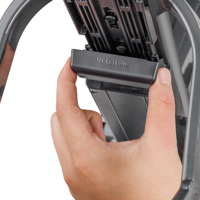 A hand fitting the Velotric battery connector cover onto the battery rail of a Velotric eBike