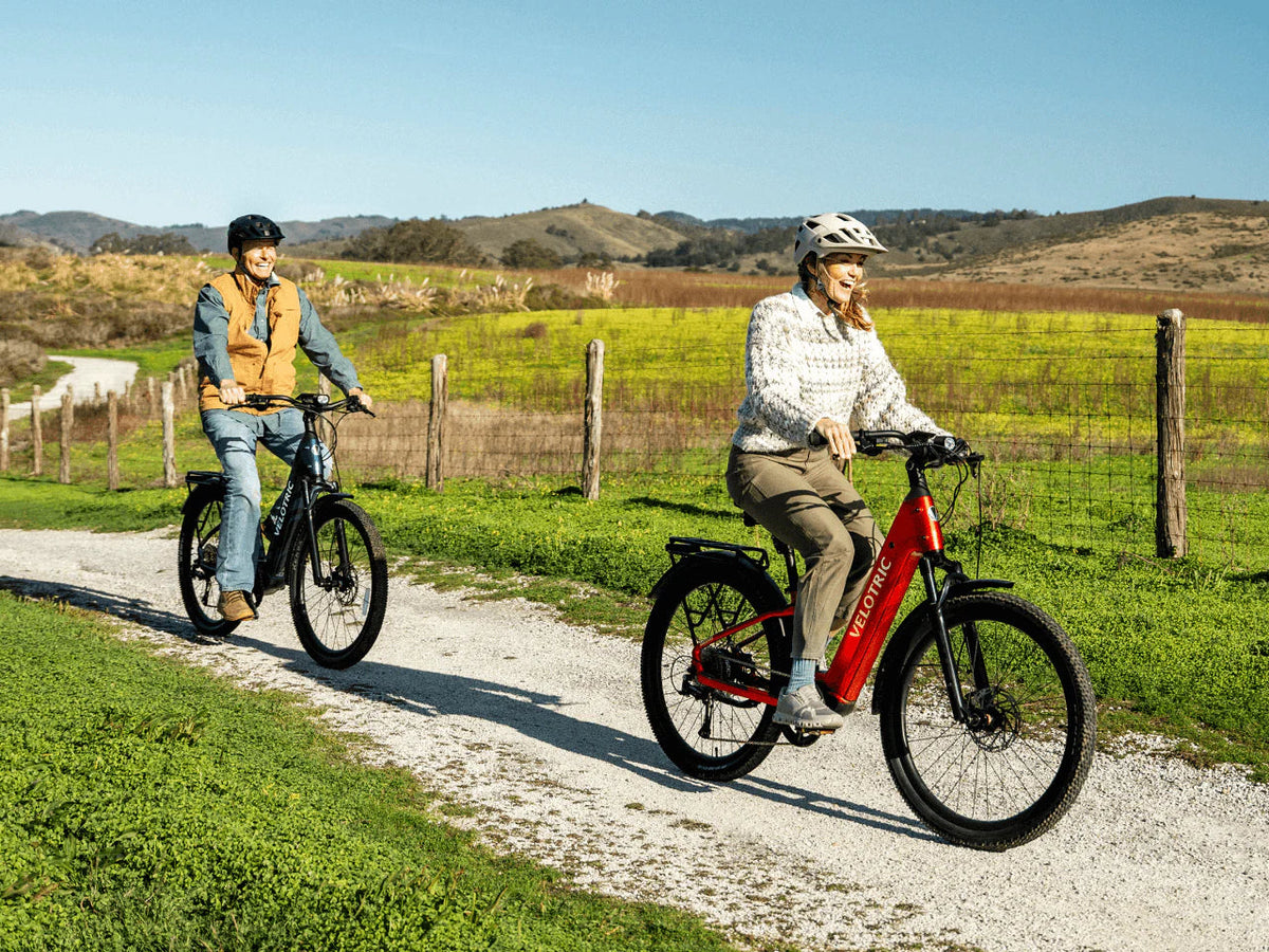 Two riders on Velotric Discover 3 e-bikes on a gravel farm road (Velotric photo) — Zeus eBikes Canada
