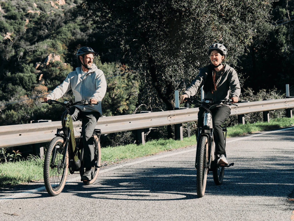 Two riders on Velotric Discover M e-bikes on a paved path lined with trees (Velotric photo) — Zeus eBikes Canada